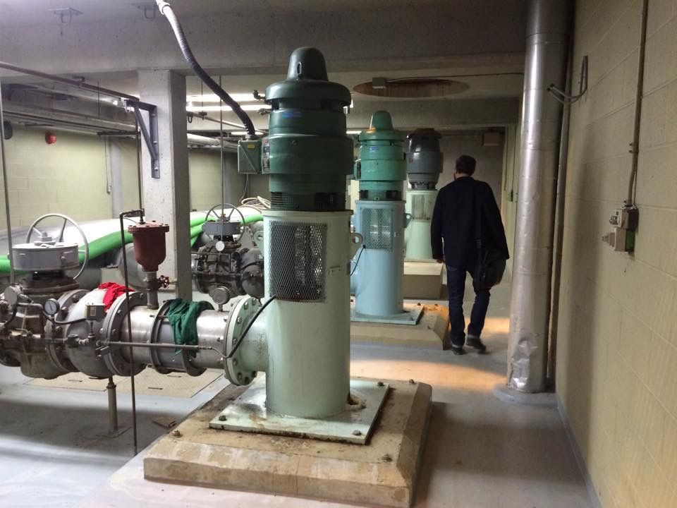 Une personne passe devant des pompes à eau industrielles dans une pièce en béton.