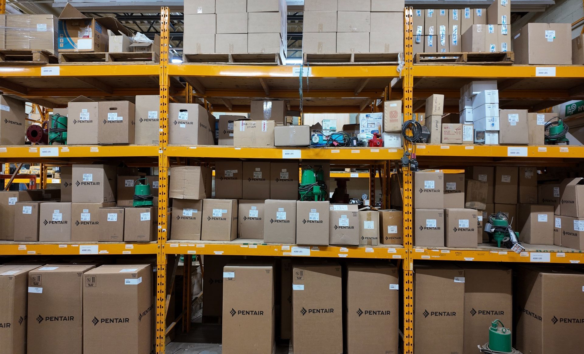Des rayonnages d'entrepôt remplis de cartons de tailles diverses, rangés sur des étagères métalliques jaunes.