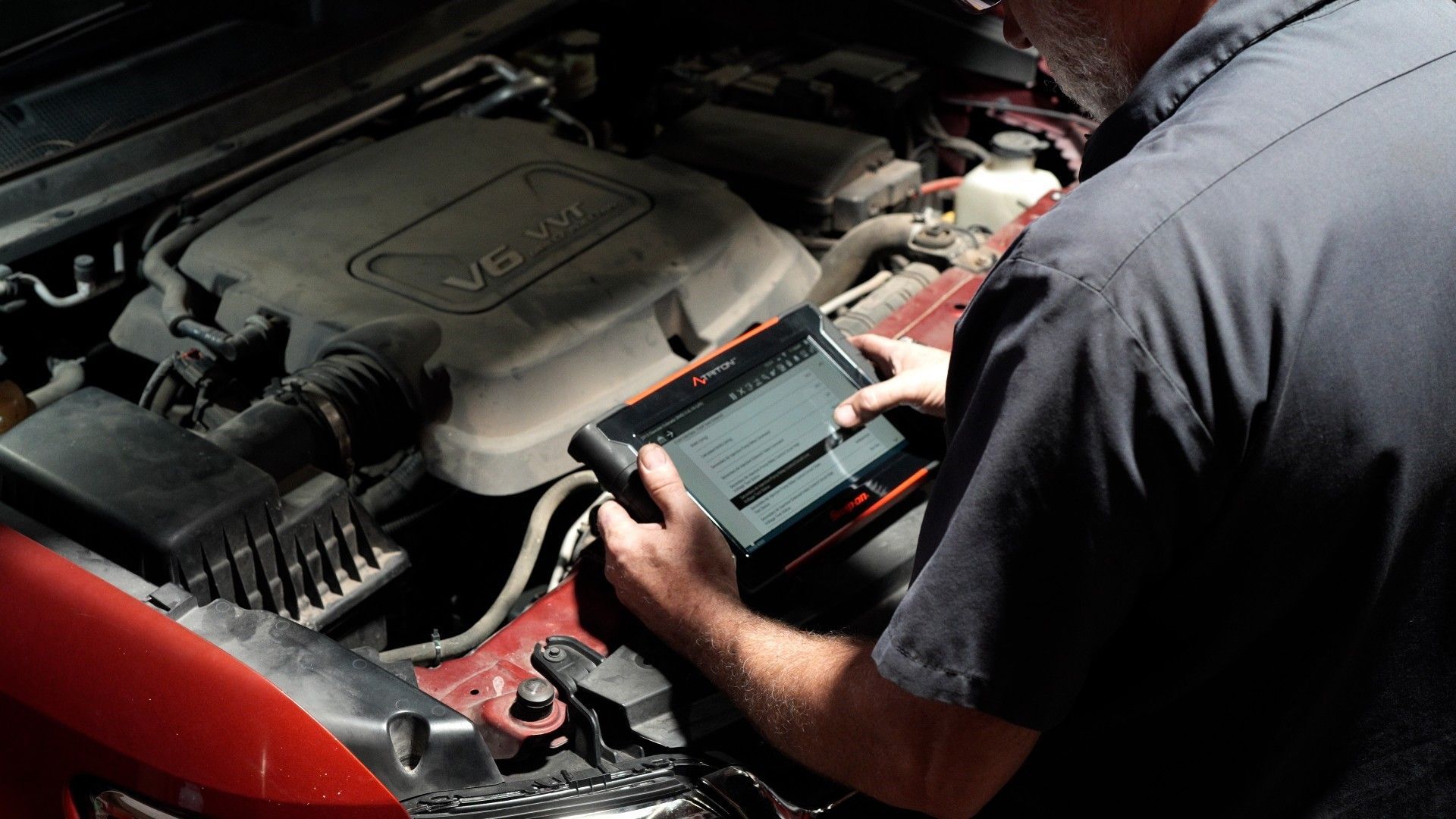 Mechanic using a handheld scanner to diagnose a car engine under the hood
