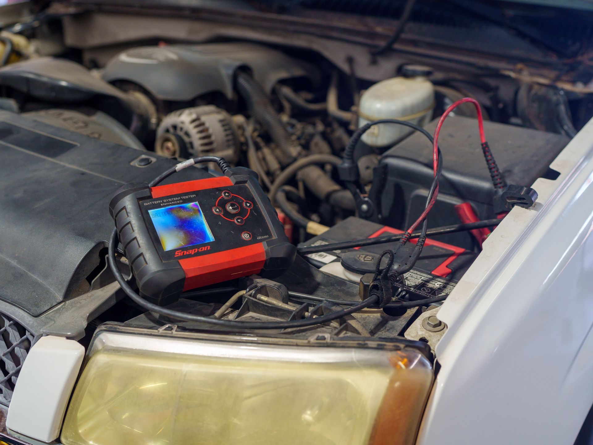Car battery jump starter connected to a car battery under the hood, with red and black cables visible.
