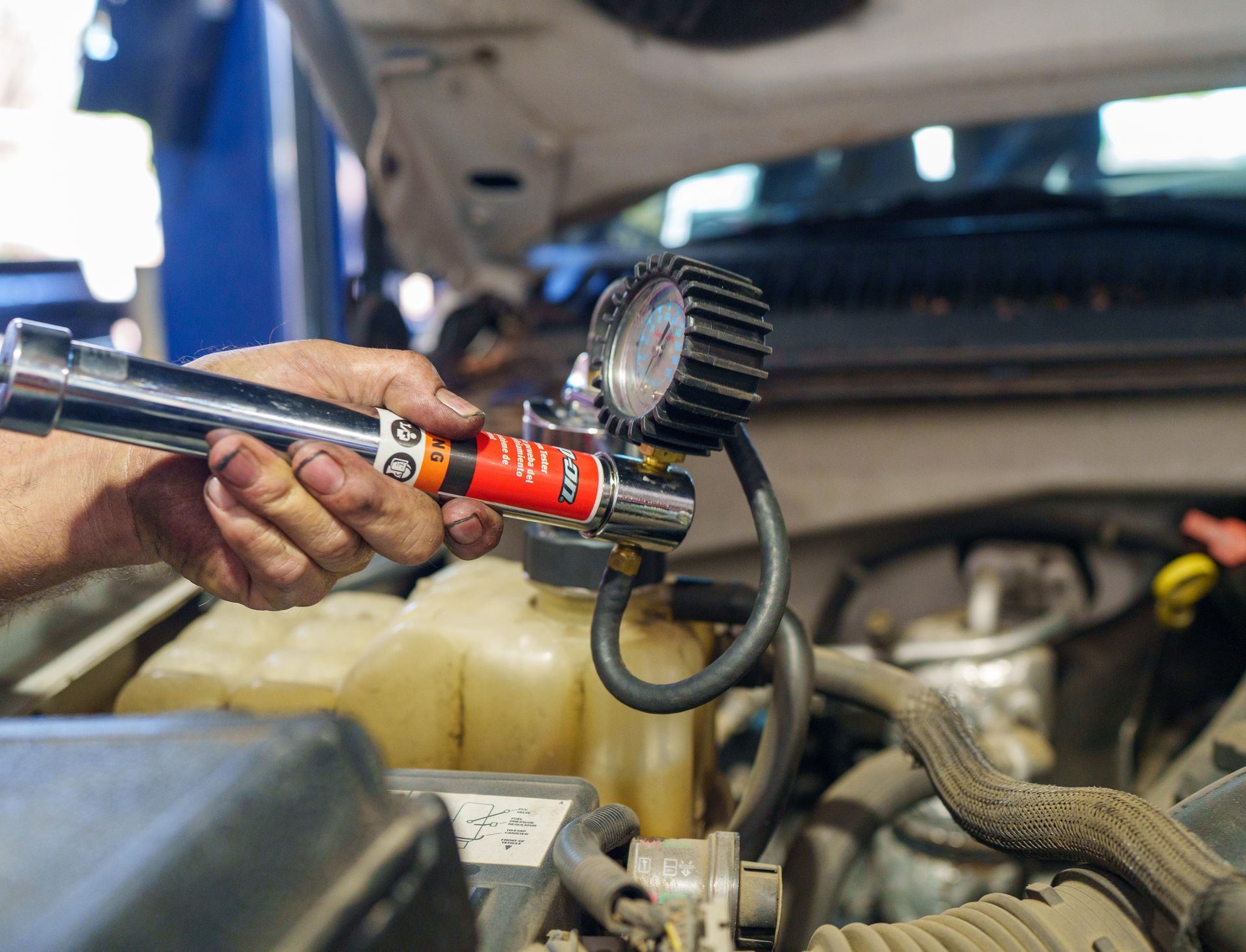 A hand uses a tire inflator to fill a car tire in an open engine bay.