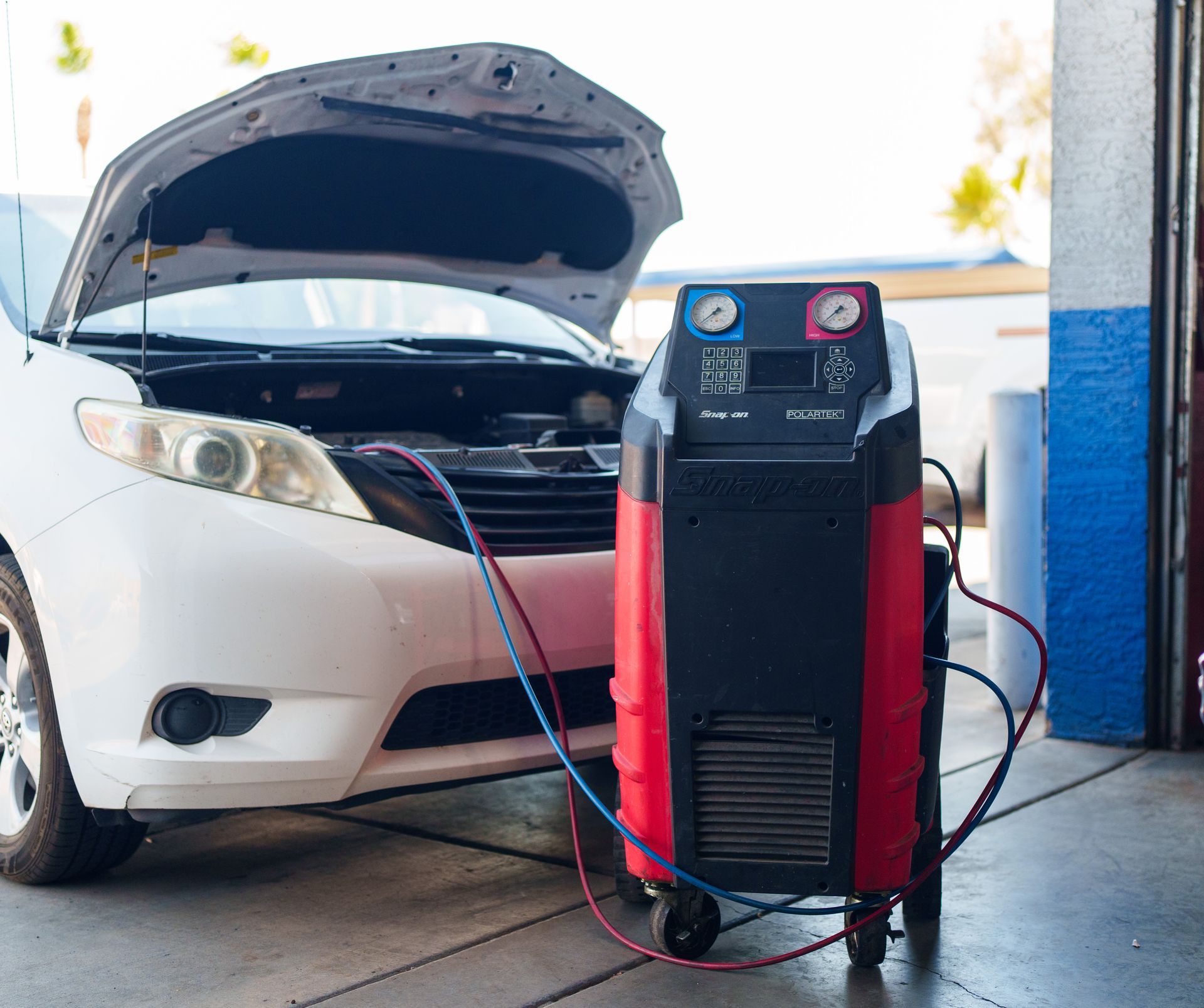 White car with open hood connected by cables to a red-and-black battery charger in a garage