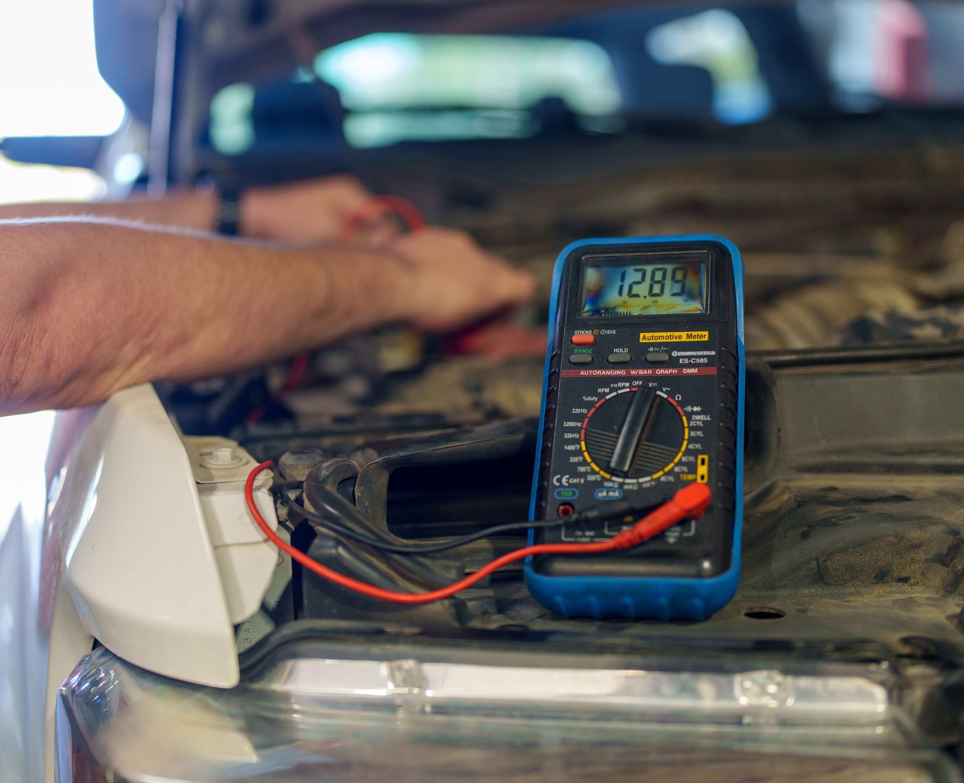 Hand using a multimeter to test a car battery in an engine bay