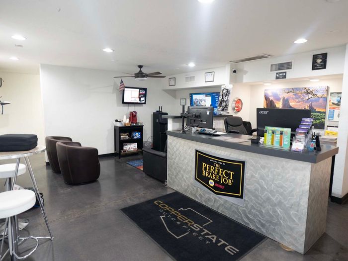 Small lobby or reception area with gray counter, chairs, TV, ceiling fan, and dark floor mats