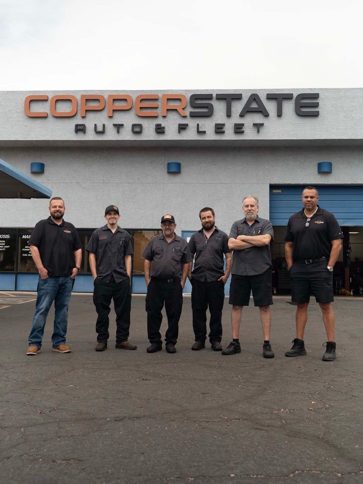 Seven people standing outside Copperstate Auto & Fleet building with arms crossed