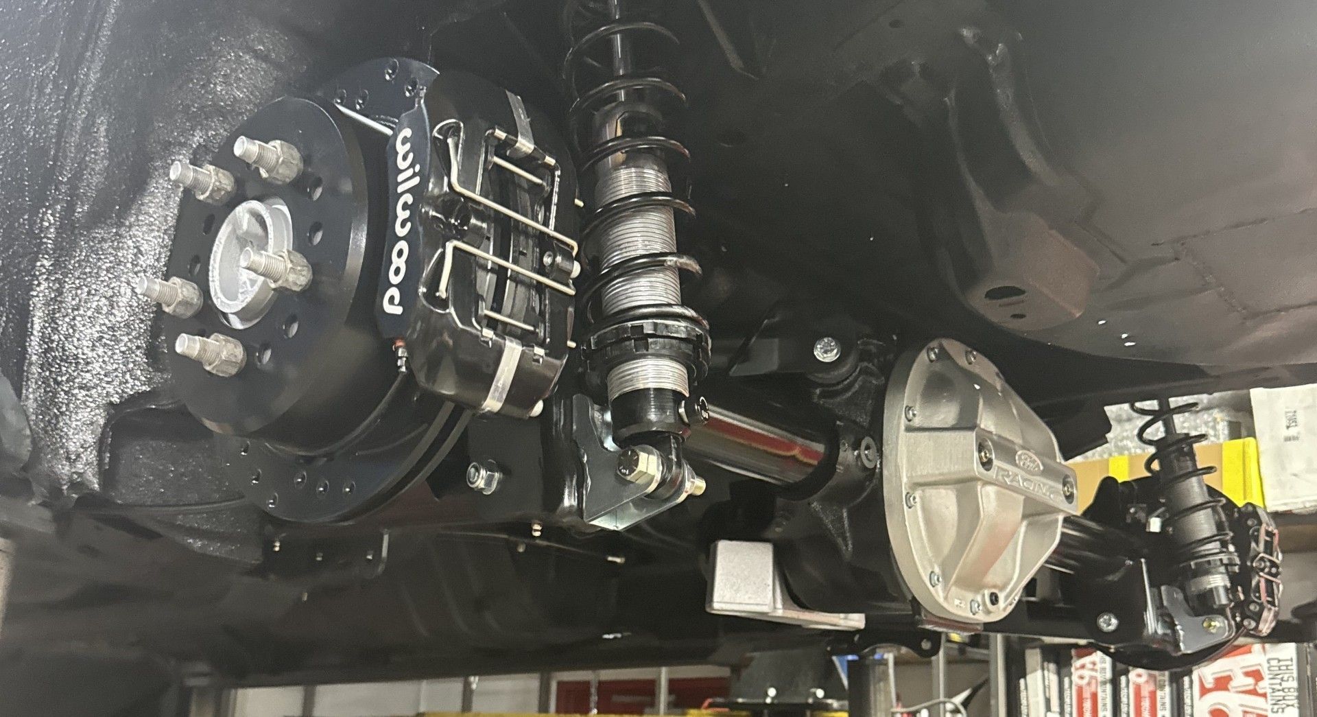 Undercarriage of a vehicle showing suspension, differential, and drivetrain components in a garage lift