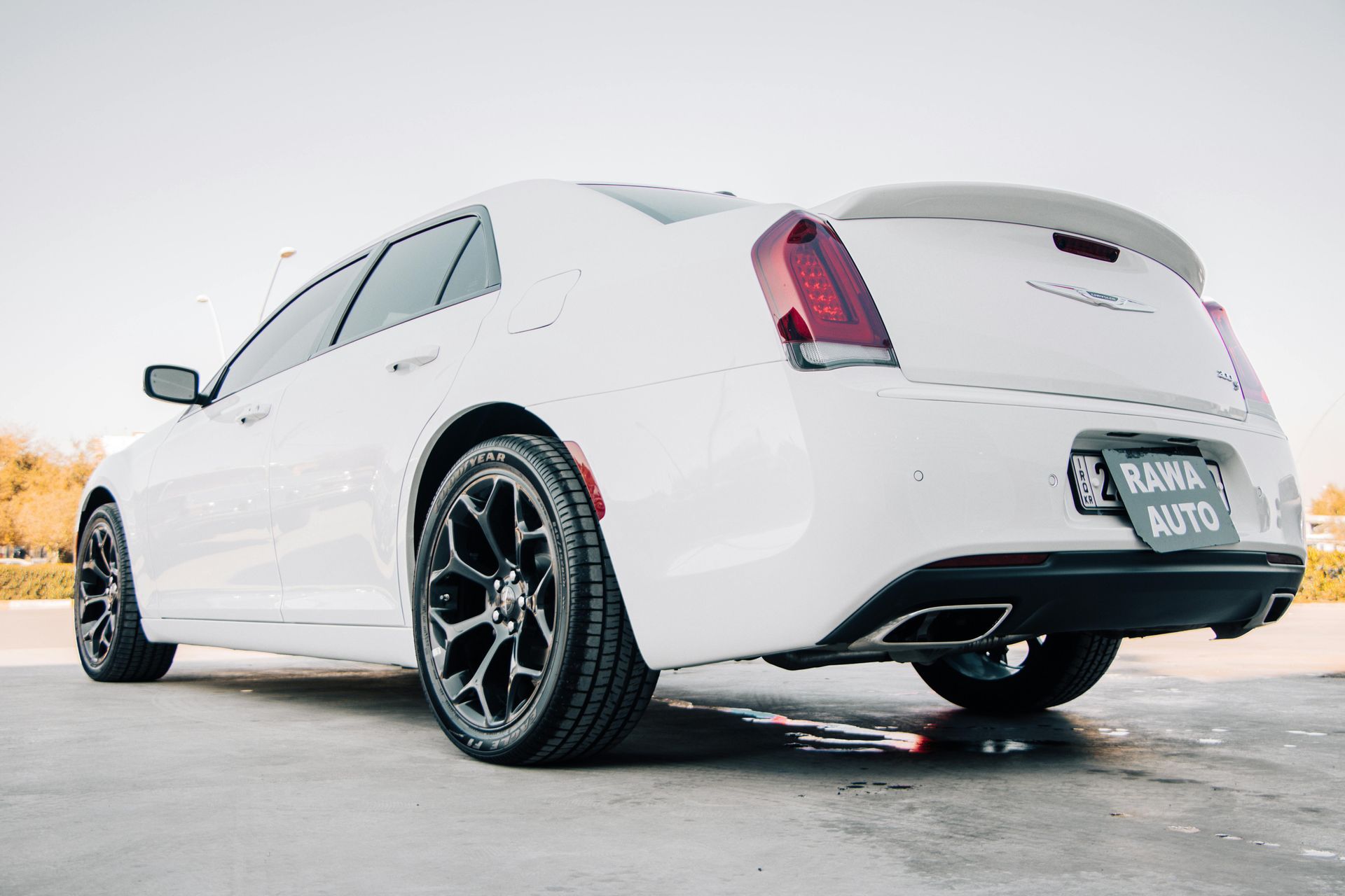 White luxury coupe seen from rear on a wet road, with black wheels and tinted windows.