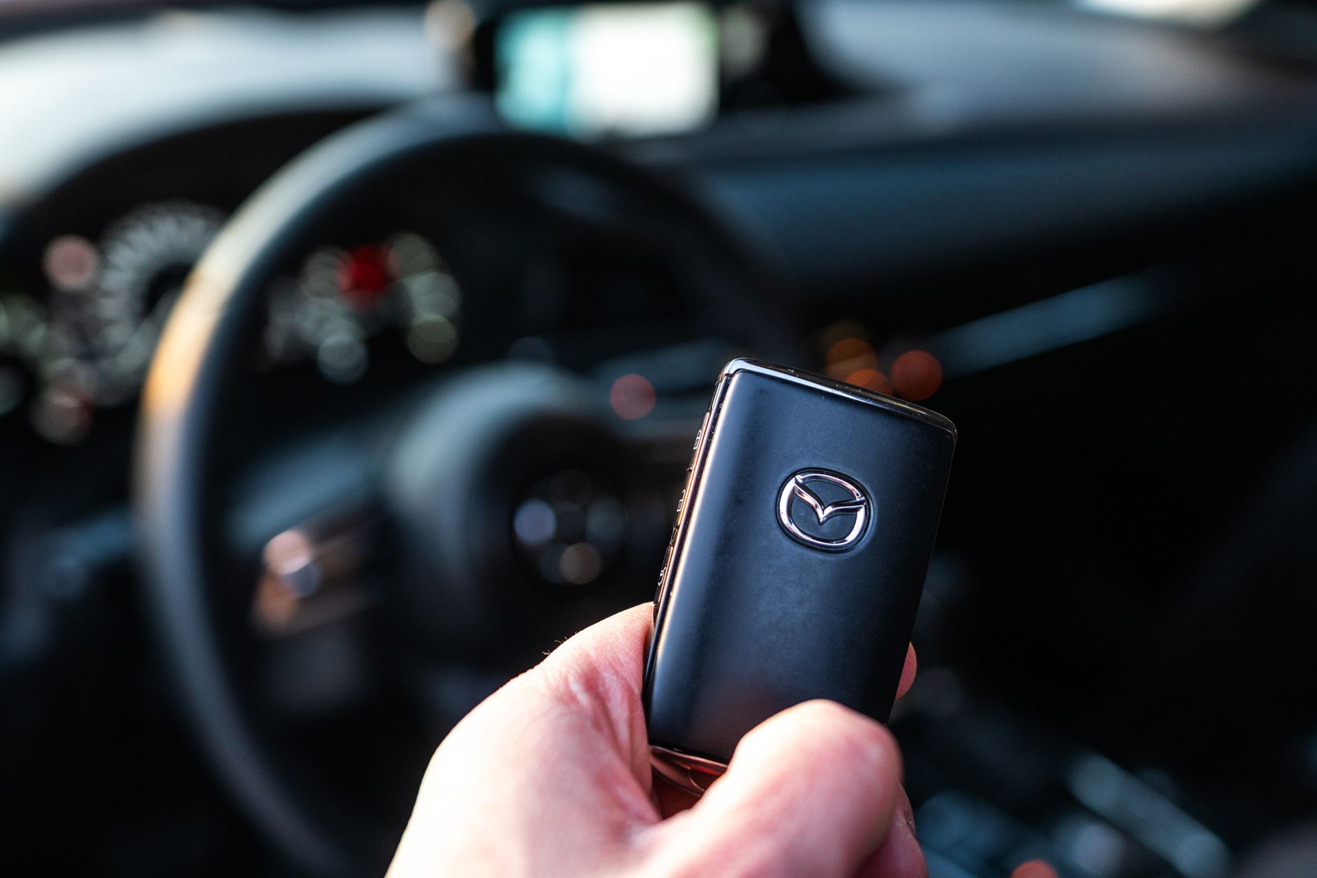 Hand holding a black Mazda car key fob inside a vehicle, with the dashboard blurred in the background