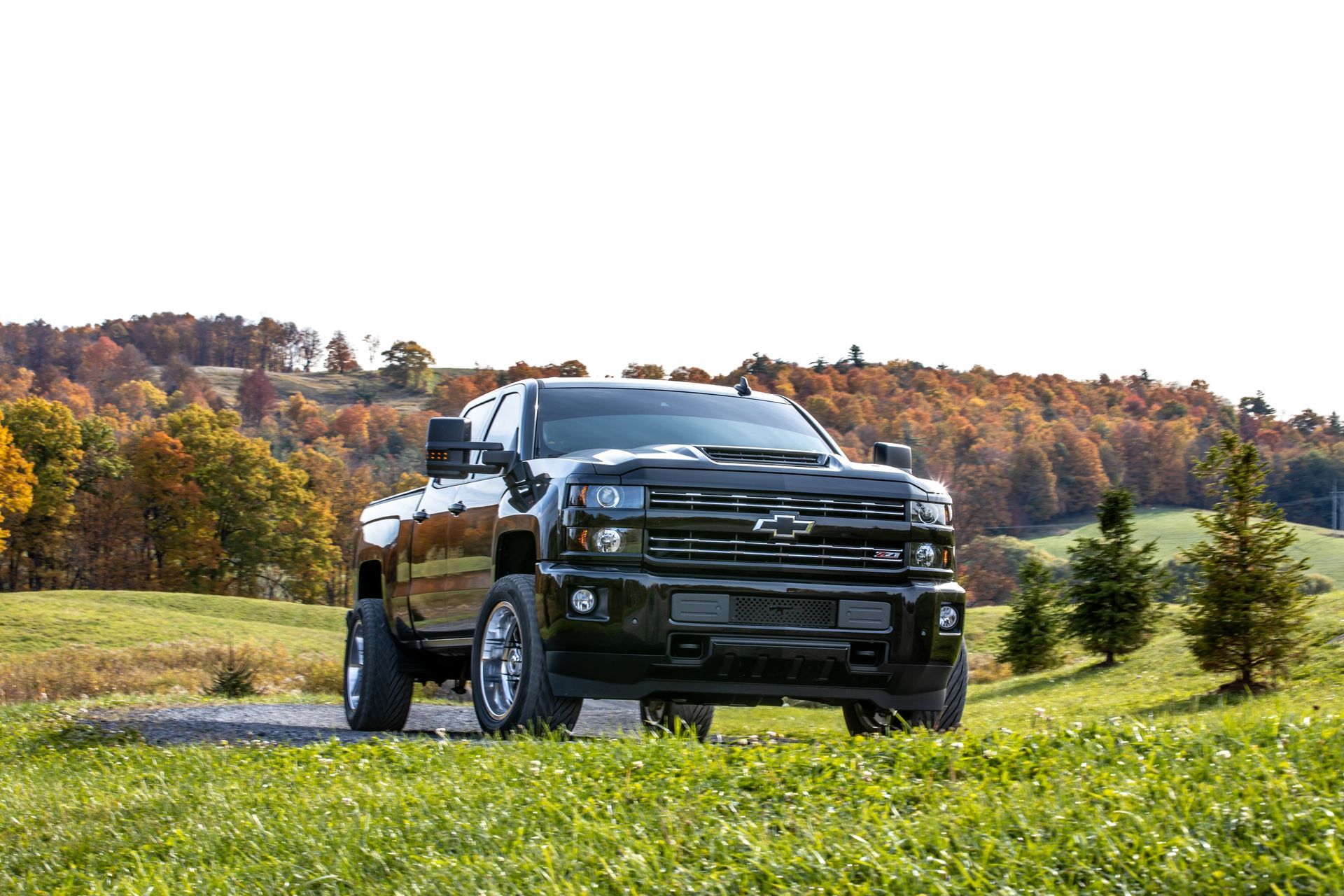 Black pickup truck driving on a grassy field with autumn trees and hills in the background