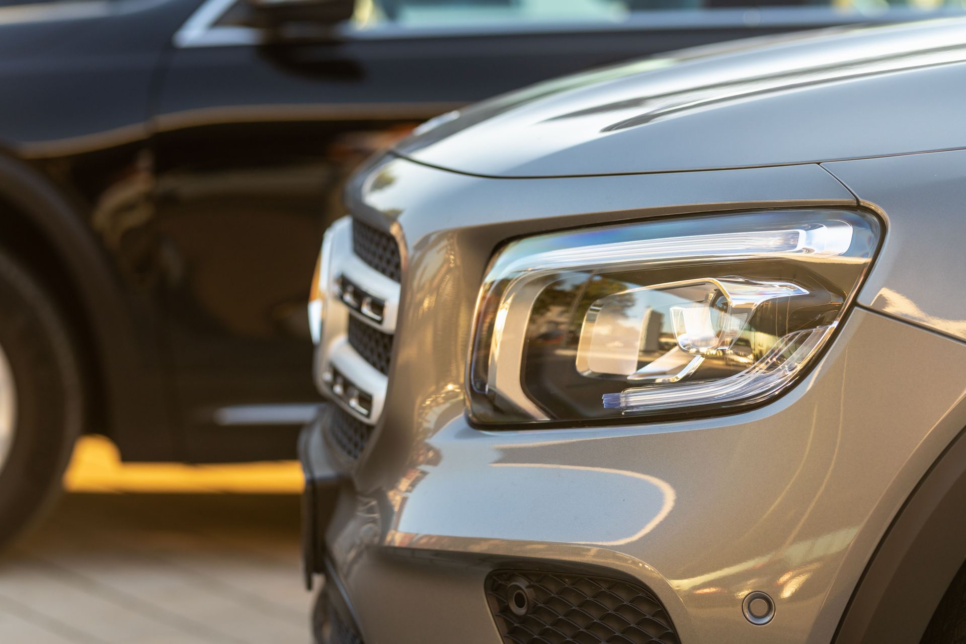 Close-up of two parked cars, with a silver SUV in the foreground and a dark car behind it.