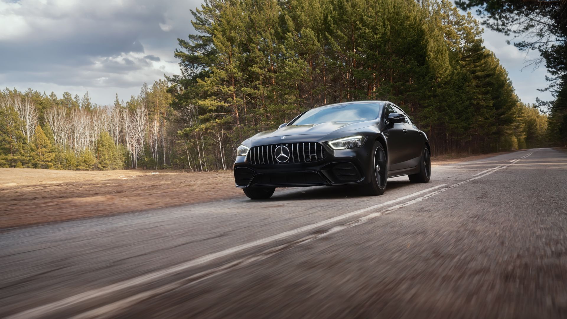 Black sports car driving on a rural road beside trees and fields