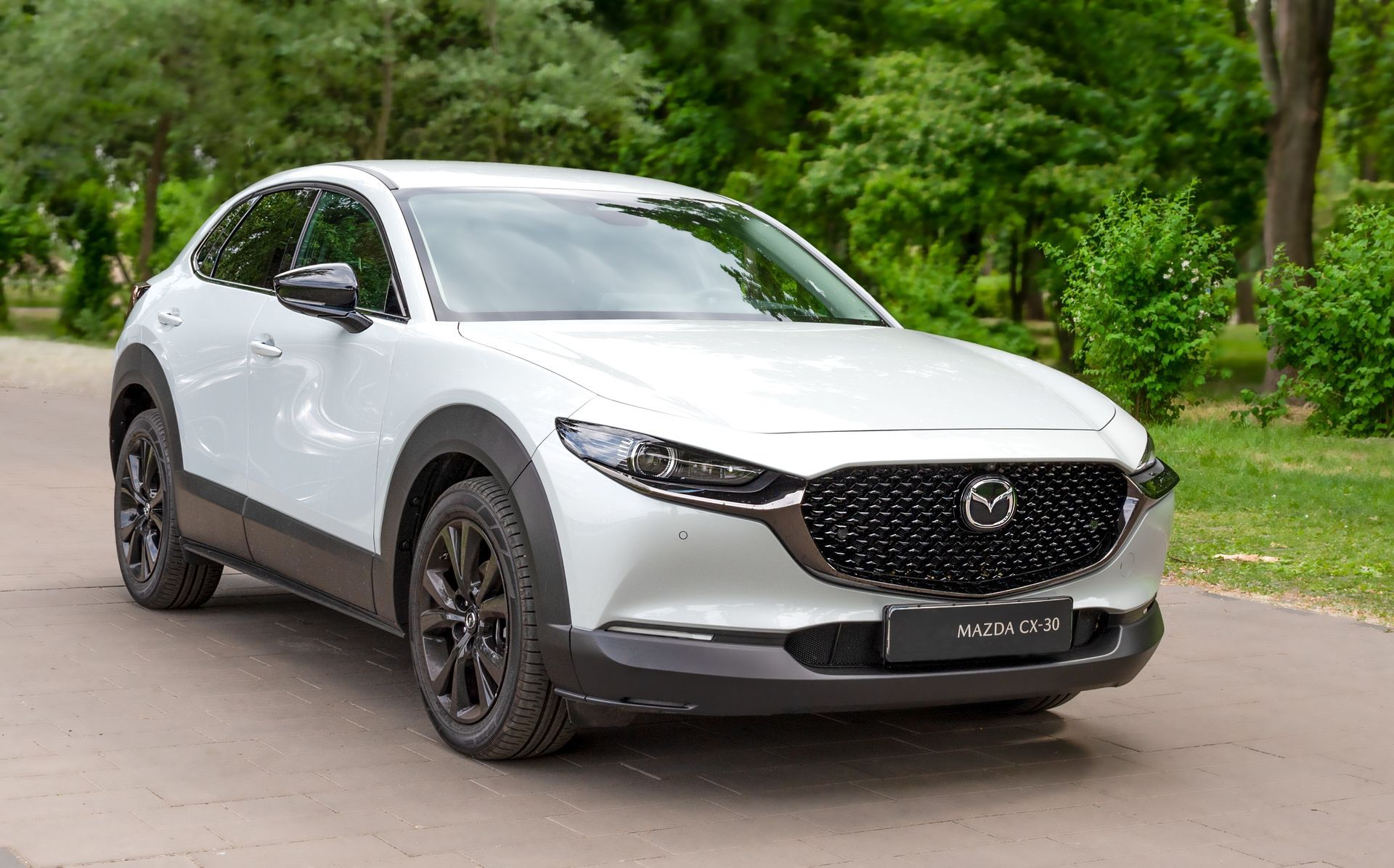 White Mazda SUV parked on a road beside lush green trees
