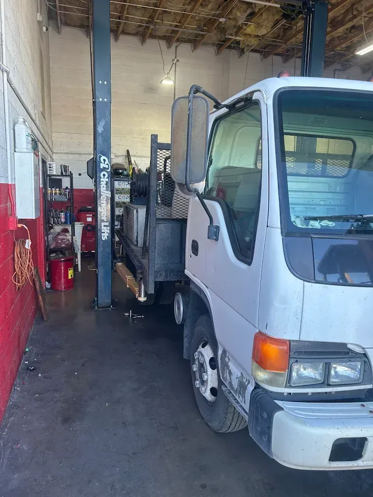 White flatbed tow truck inside an auto shop bay, with red equipment and a lift in the background