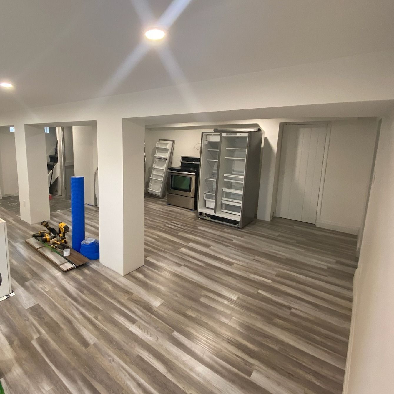 Empty unfinished room with gray wood floors, white walls, and stacked construction supplies near the back wall
