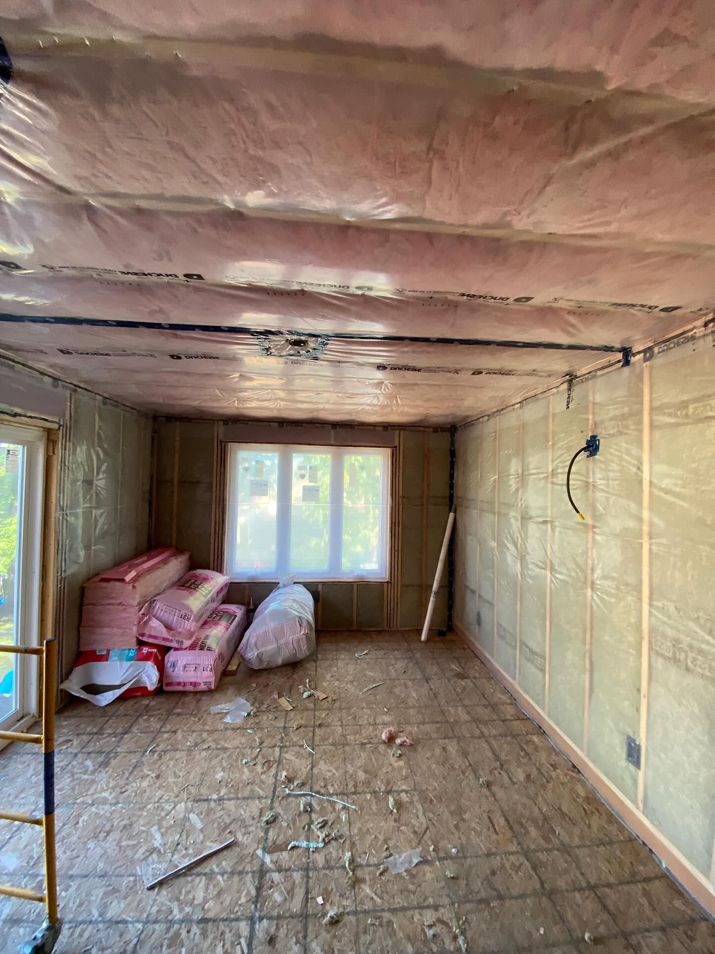 Unfinished room with insulation, exposed ceiling, stacked bags, and a window at the far end.