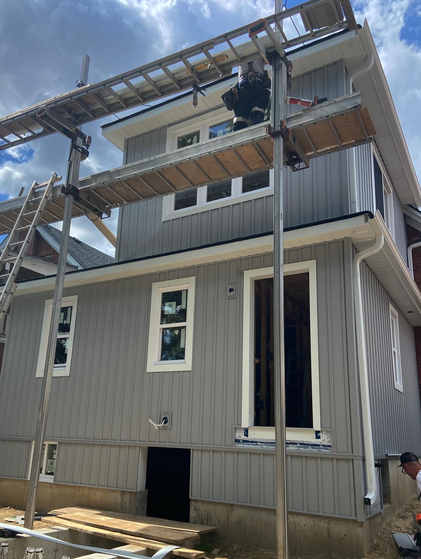 Partially finished gray two-story house with scaffolding and ladders against a blue sky