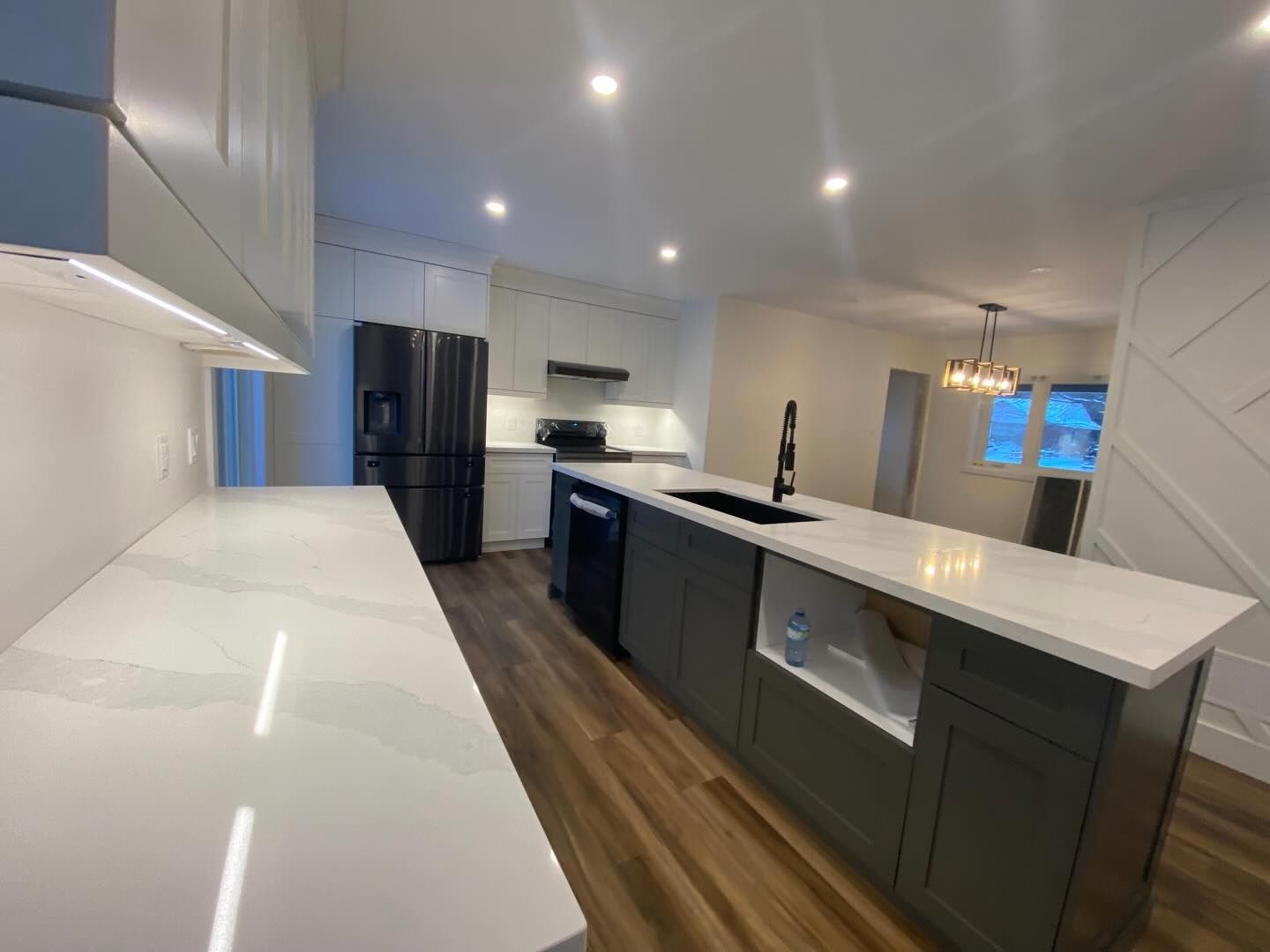 Modern white kitchen with dark island, stainless appliances, wood floor, and recessed lighting