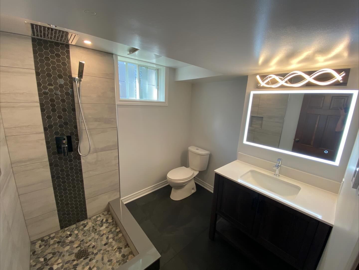 Modern bathroom with tiled shower, toilet, and vanity with lit mirror