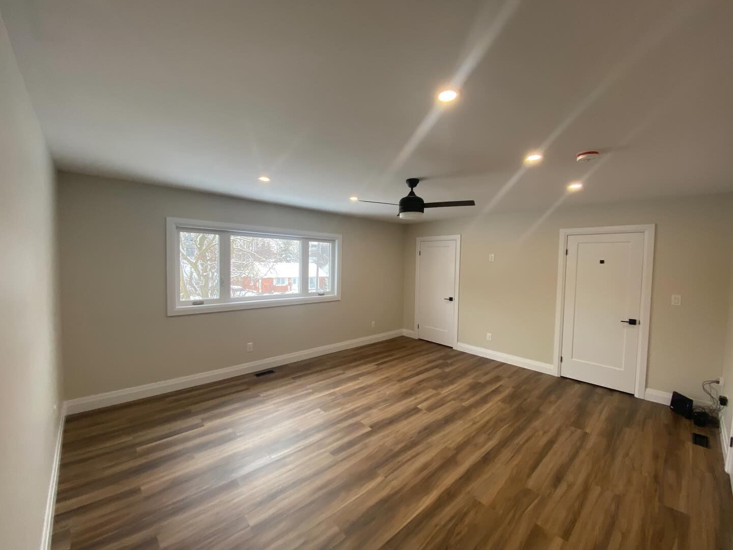 Empty living room with wood floors, white walls, recessed lights, a ceiling fan, and a window.
