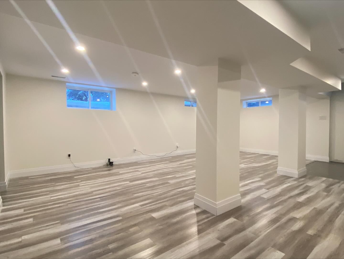 Empty modern room with white walls, wood-pattern flooring, recessed lights, and small high windows.