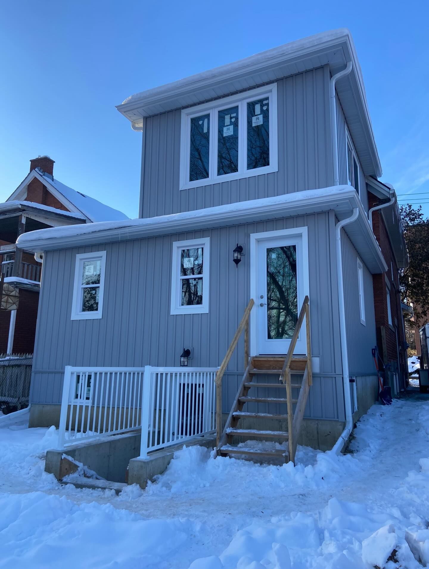 Snow-covered gray two-story house with a front porch and steps in winter.