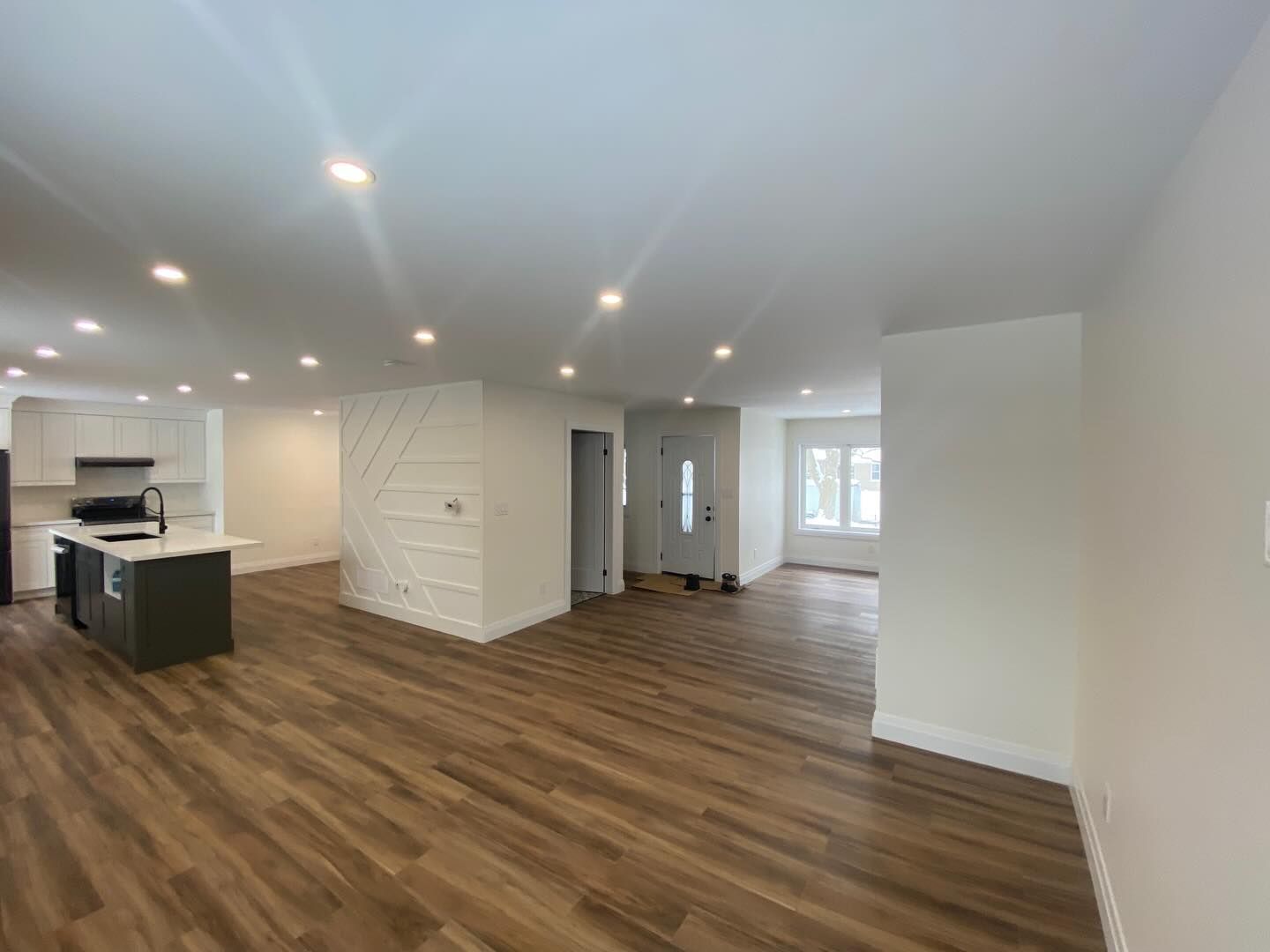 Bright open-plan room with wood floors, white walls, recessed lights, kitchen island, and windows.