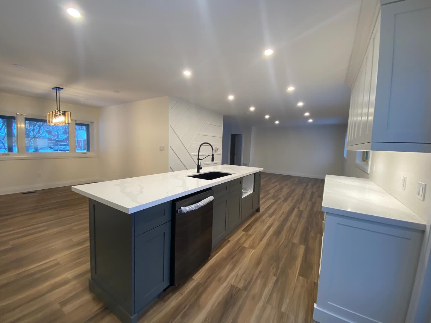 Modern kitchen with white island, dark cabinets, wood floors, and recessed lighting