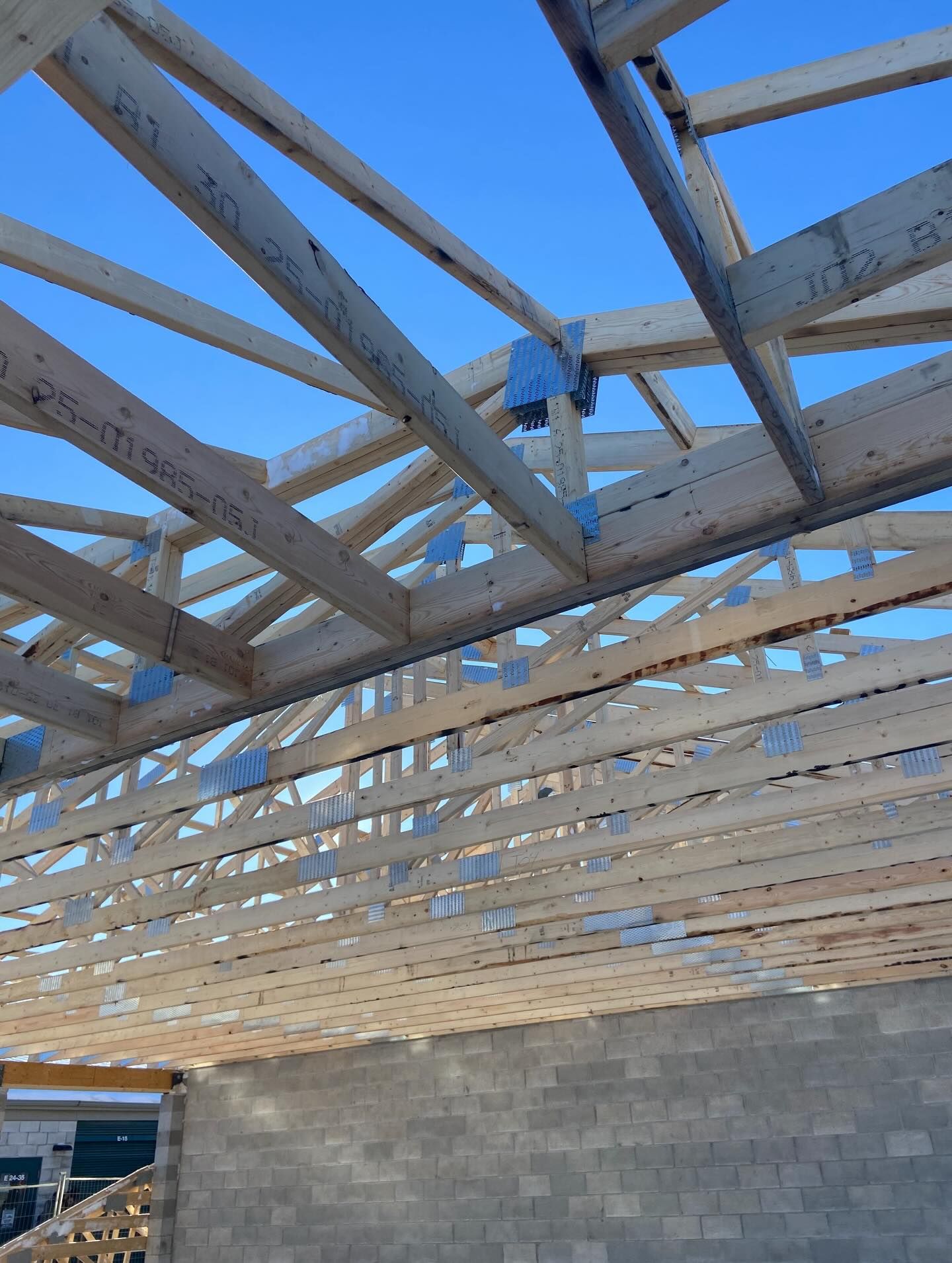 Partially built roof framing with a worker on a wooden truss over cinder block walls under a blue sky