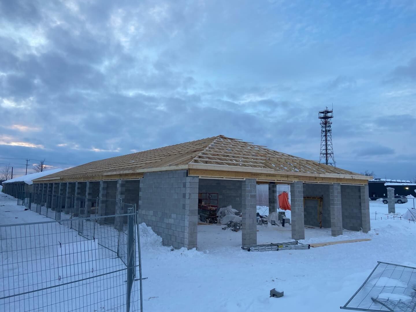 Snowy construction site with a partially built house under a cloudy sky