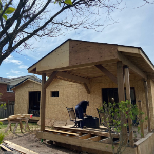 Partially built wooden porch with a worker bending over on the deck beside a brick house