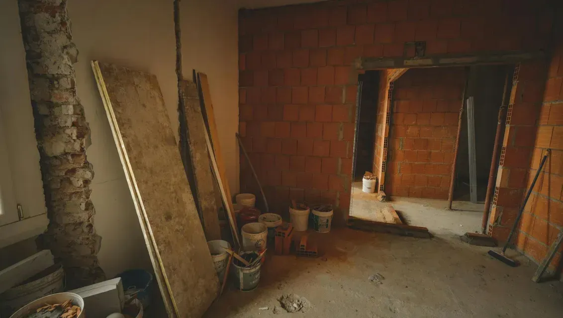 Unfinished room with exposed brick walls, construction materials, and buckets on a dusty floor.