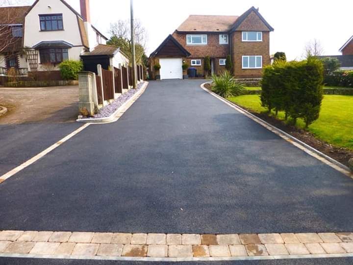 Paved driveway leading to a two-story house and garage. Brown brick edging borders driveway and a lawn.