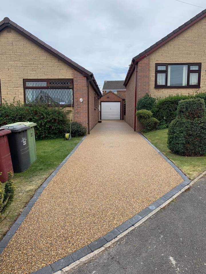 Driveway between two tan brick houses leading to a white garage.