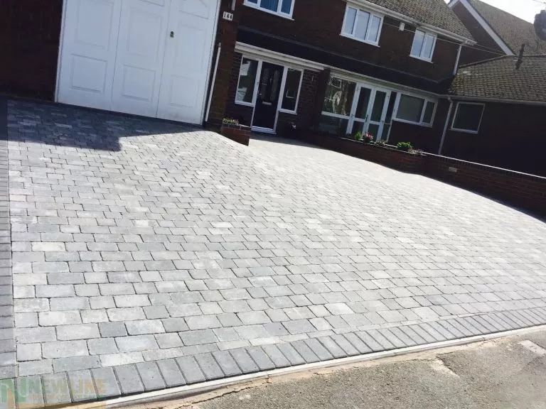 Gray brick driveway in front of a house with white garage door and front door.