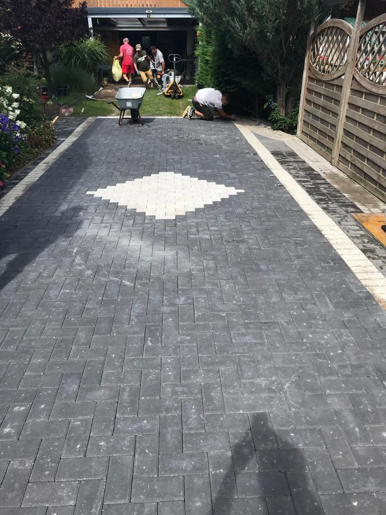 Dark gray brick driveway with a white diamond design, bordered by beige brick and a wooden fence.
