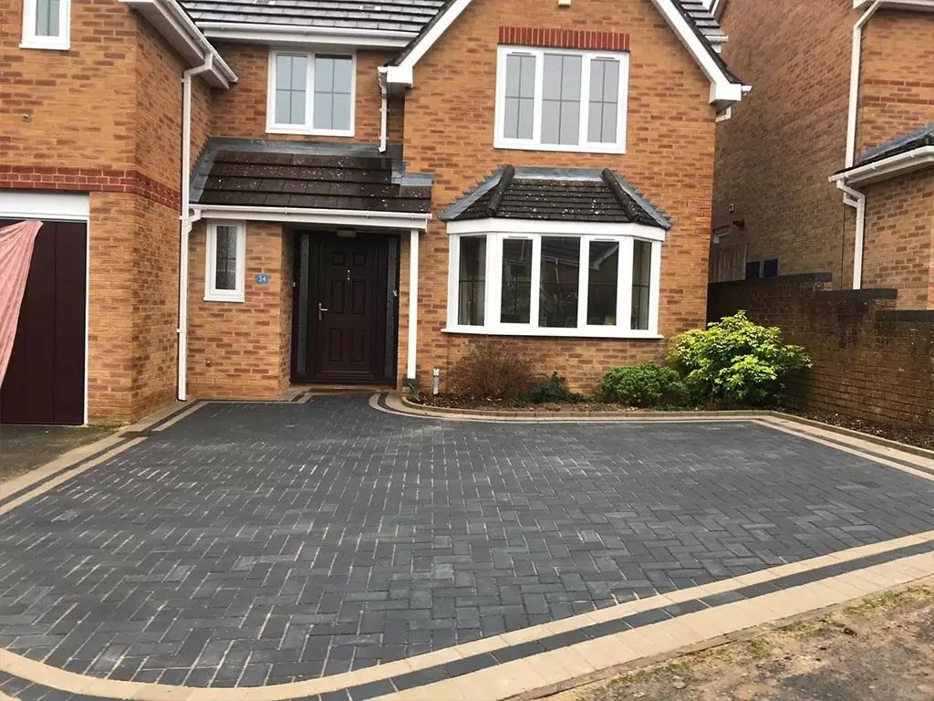 Brick house with dark gray brick paved driveway and beige border.