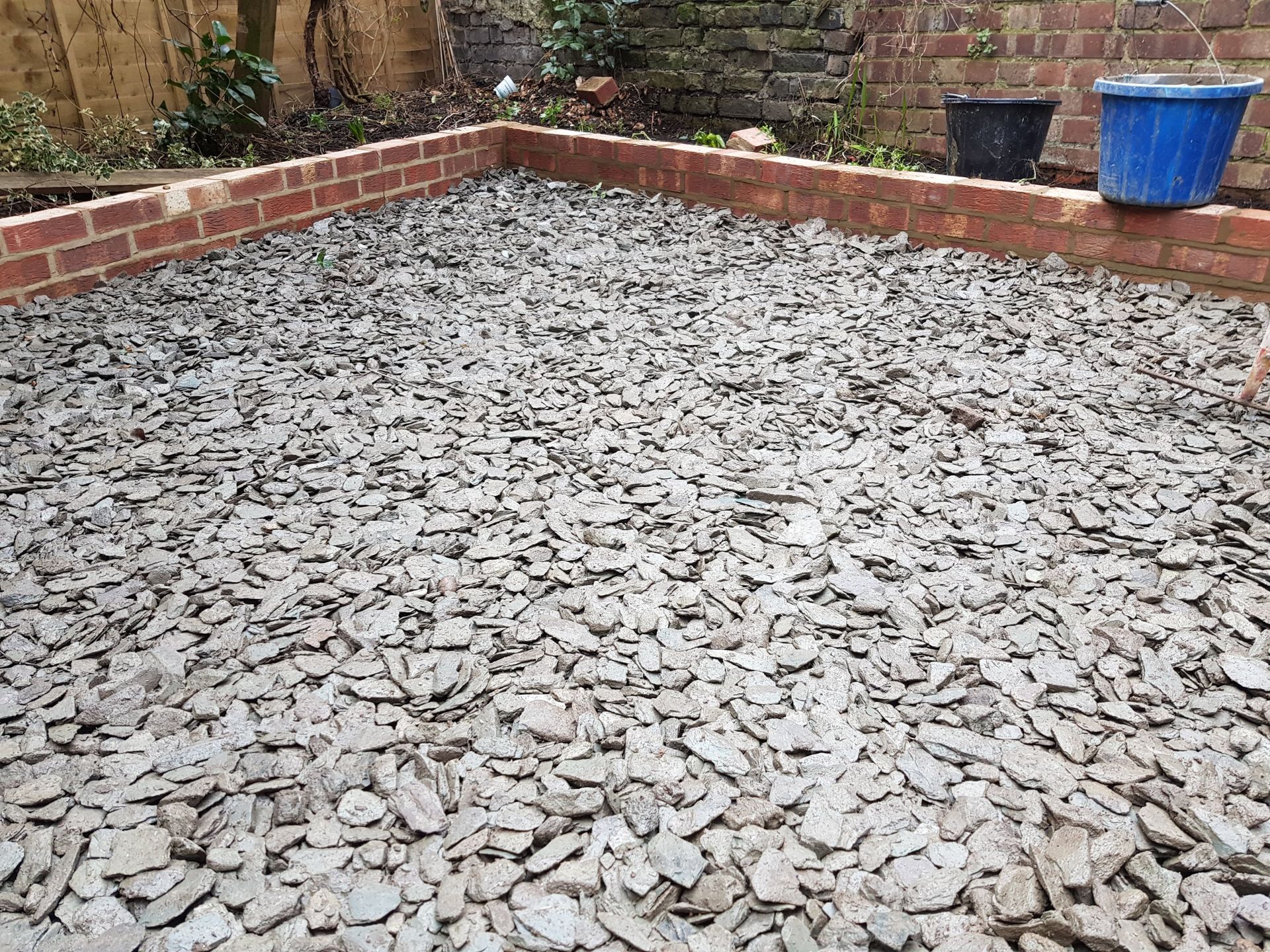 A gravel-covered patio enclosed by a brick border, with two buckets nearby.