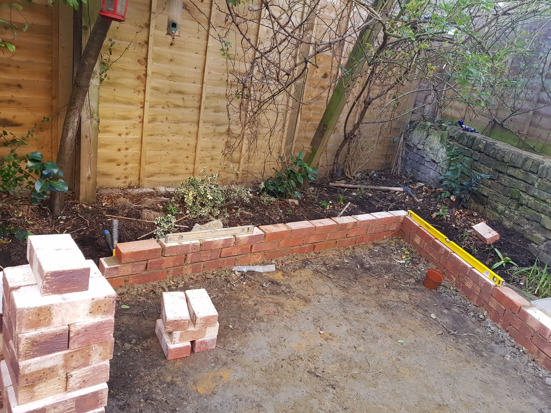 Brick wall construction in a backyard setting, with stacked bricks and unfinished walls.