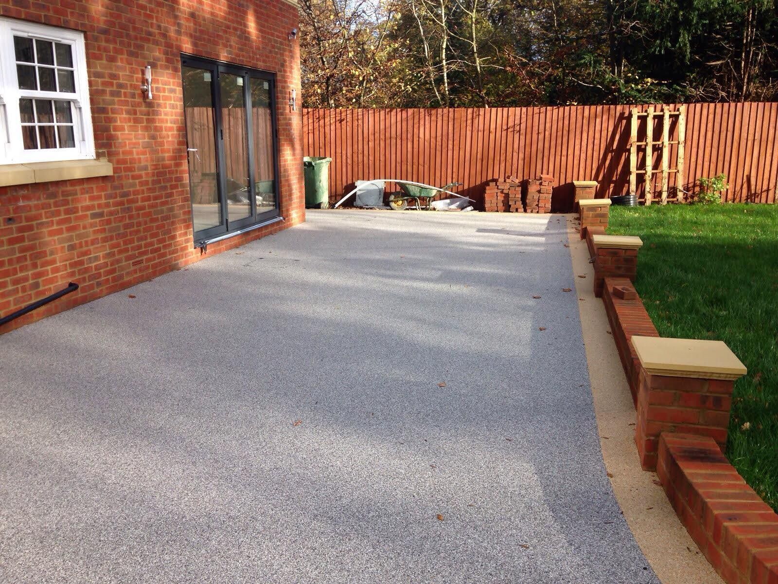 Exterior patio with gray stone surface, brick wall, and green lawn.