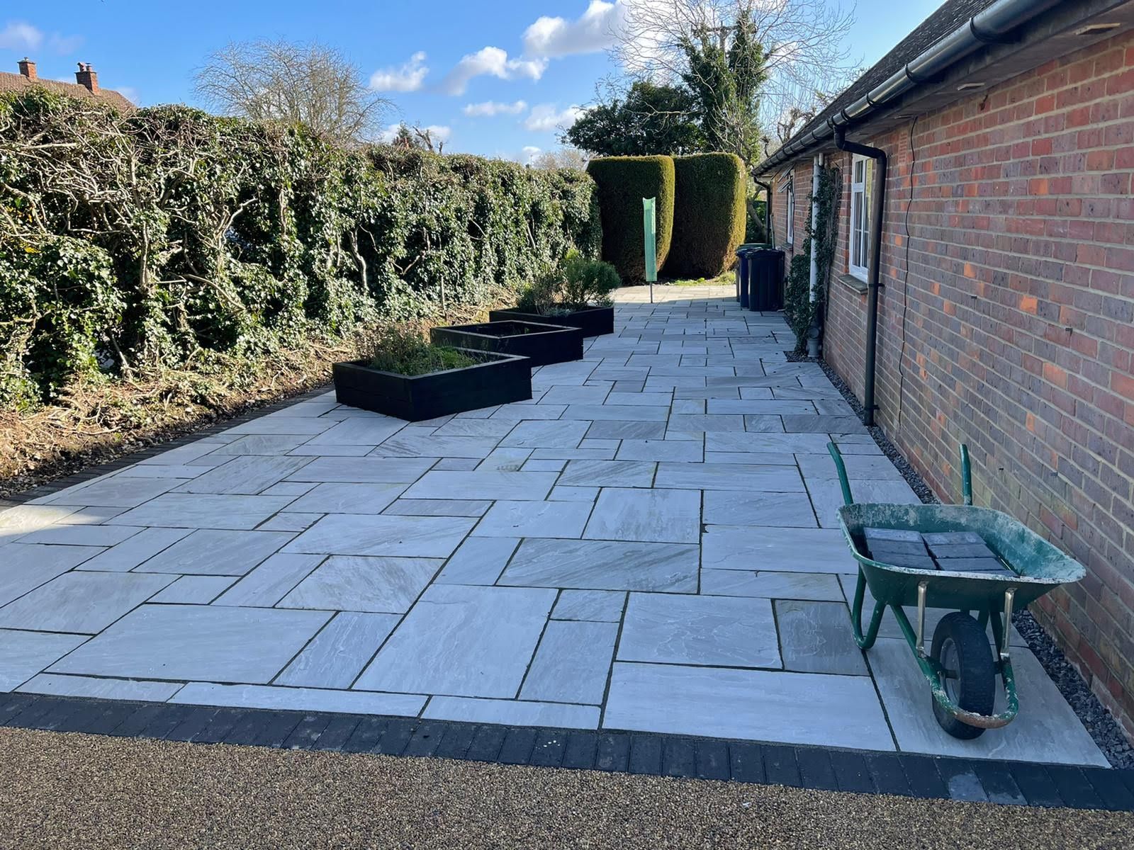 Stone patio next to brick building with planter boxes and a wheelbarrow.