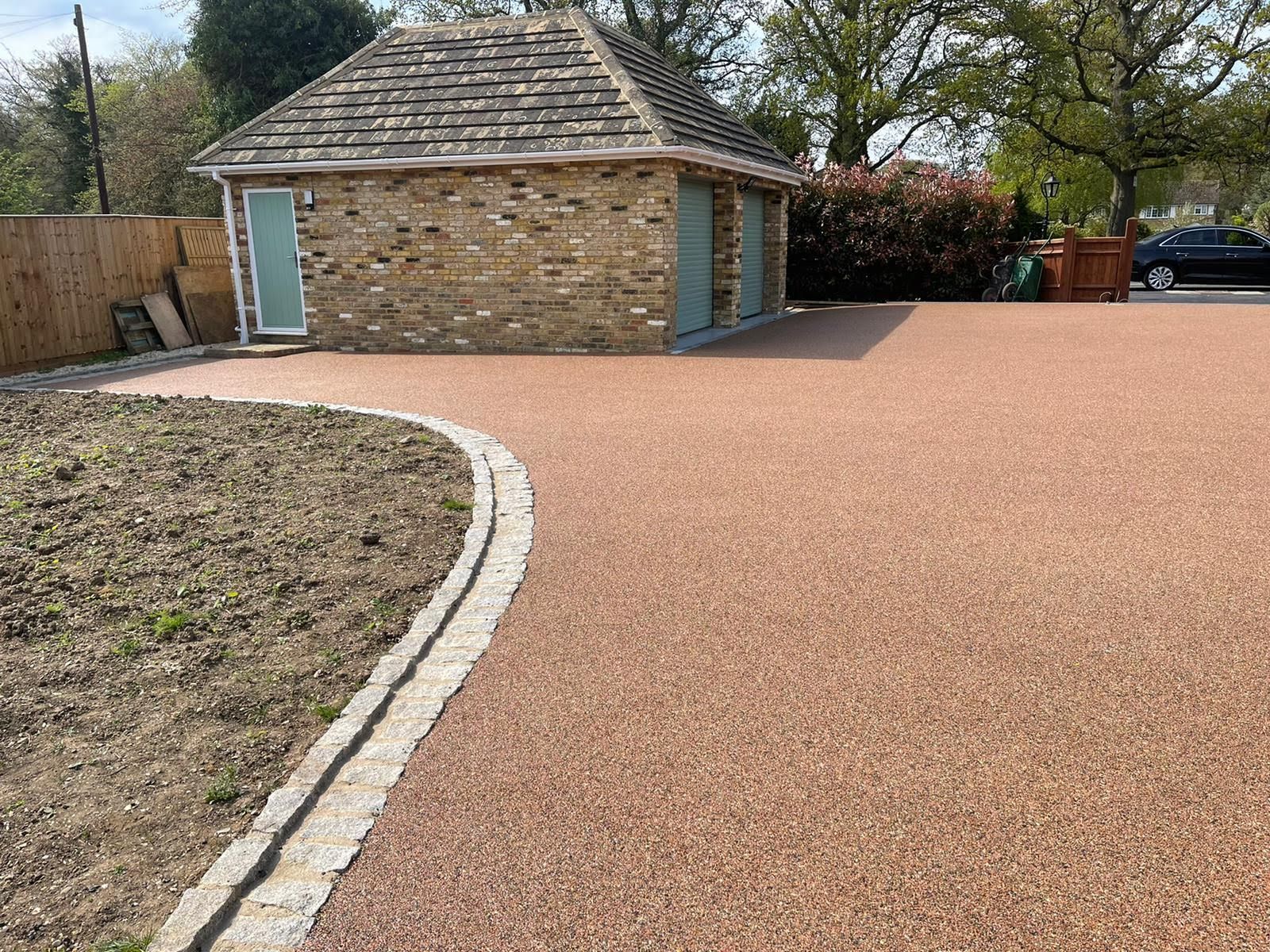 Gravel driveway next to a stone garage with a flowerbed on the left.