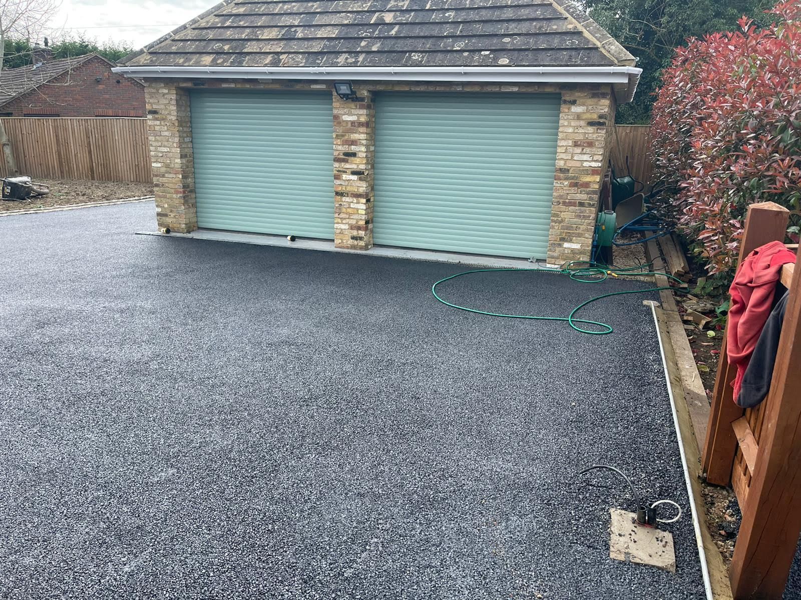 Driveway with gray gravel leading to a brick garage with two teal roller doors.