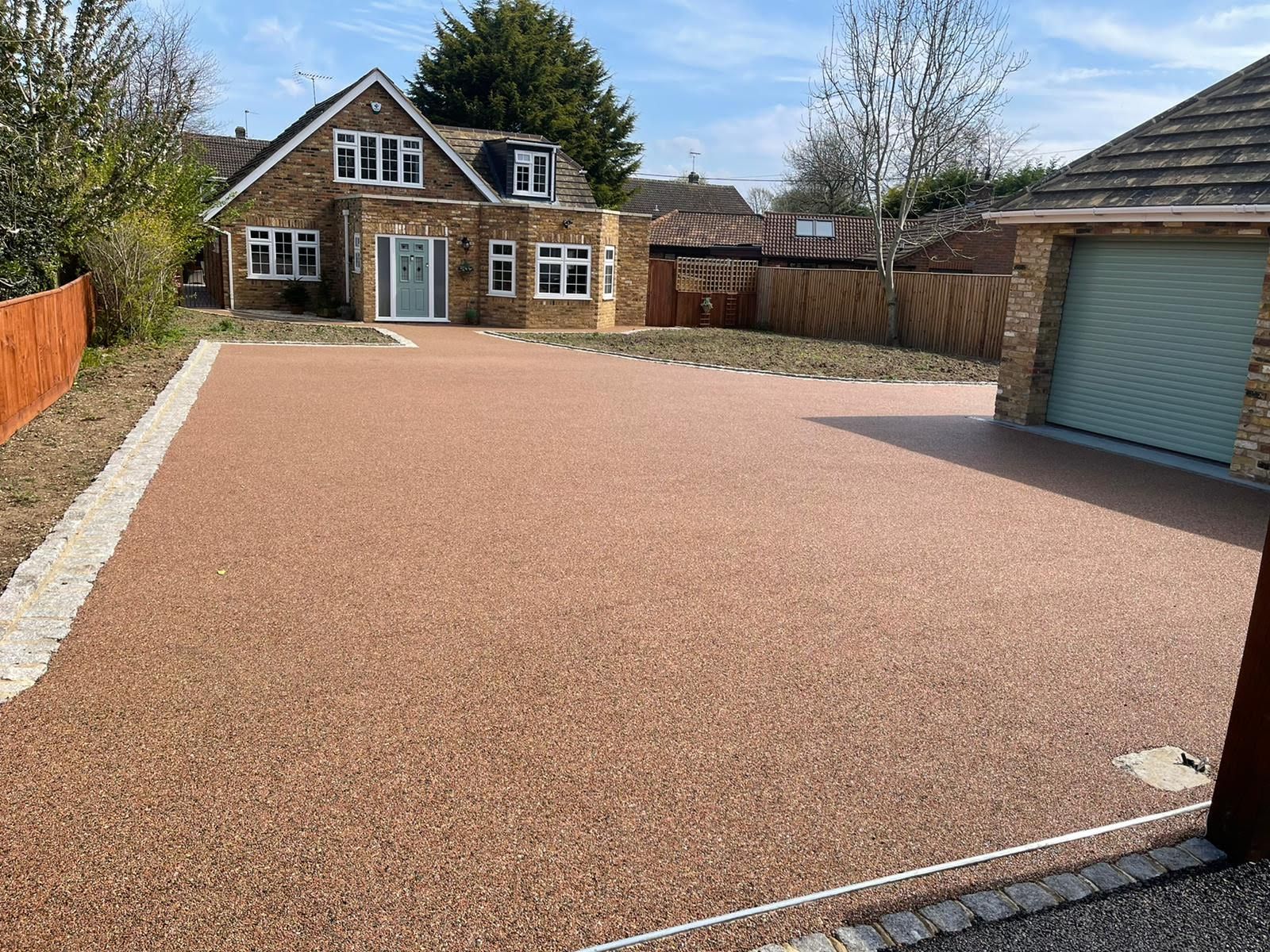 House with brown resin driveway. Garage on right, light blue front door. Beige brick house.