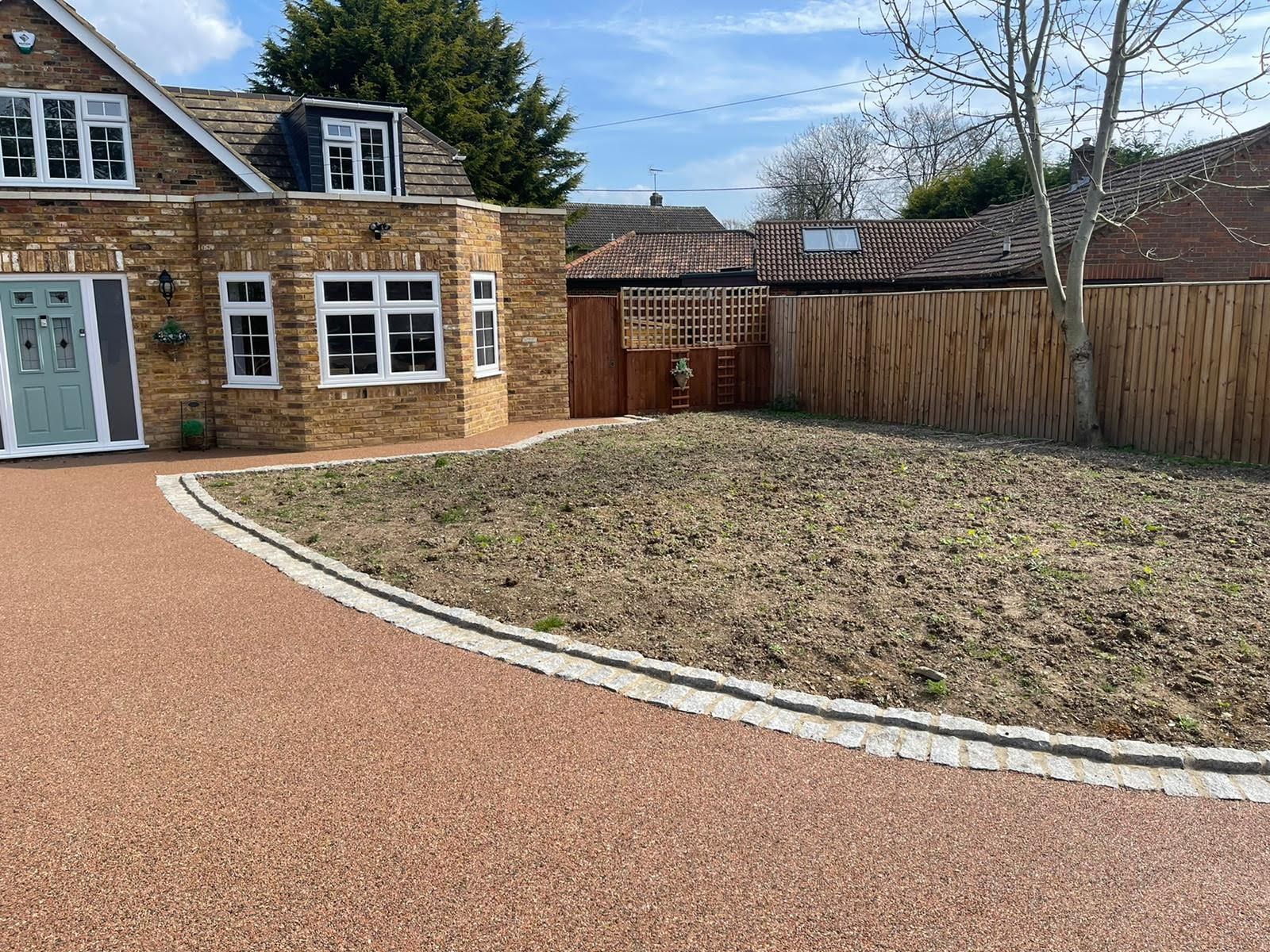 A brick house with a gravel driveway and a bare lawn. Brown bamboo fencing surrounds the yard.