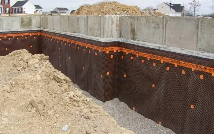 Foundation walls with brown waterproofing membrane and gravel base, awaiting backfill.