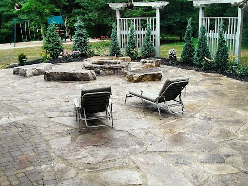 Stone patio with lounge chairs, fire pit, and landscaped garden with a playground in the background.