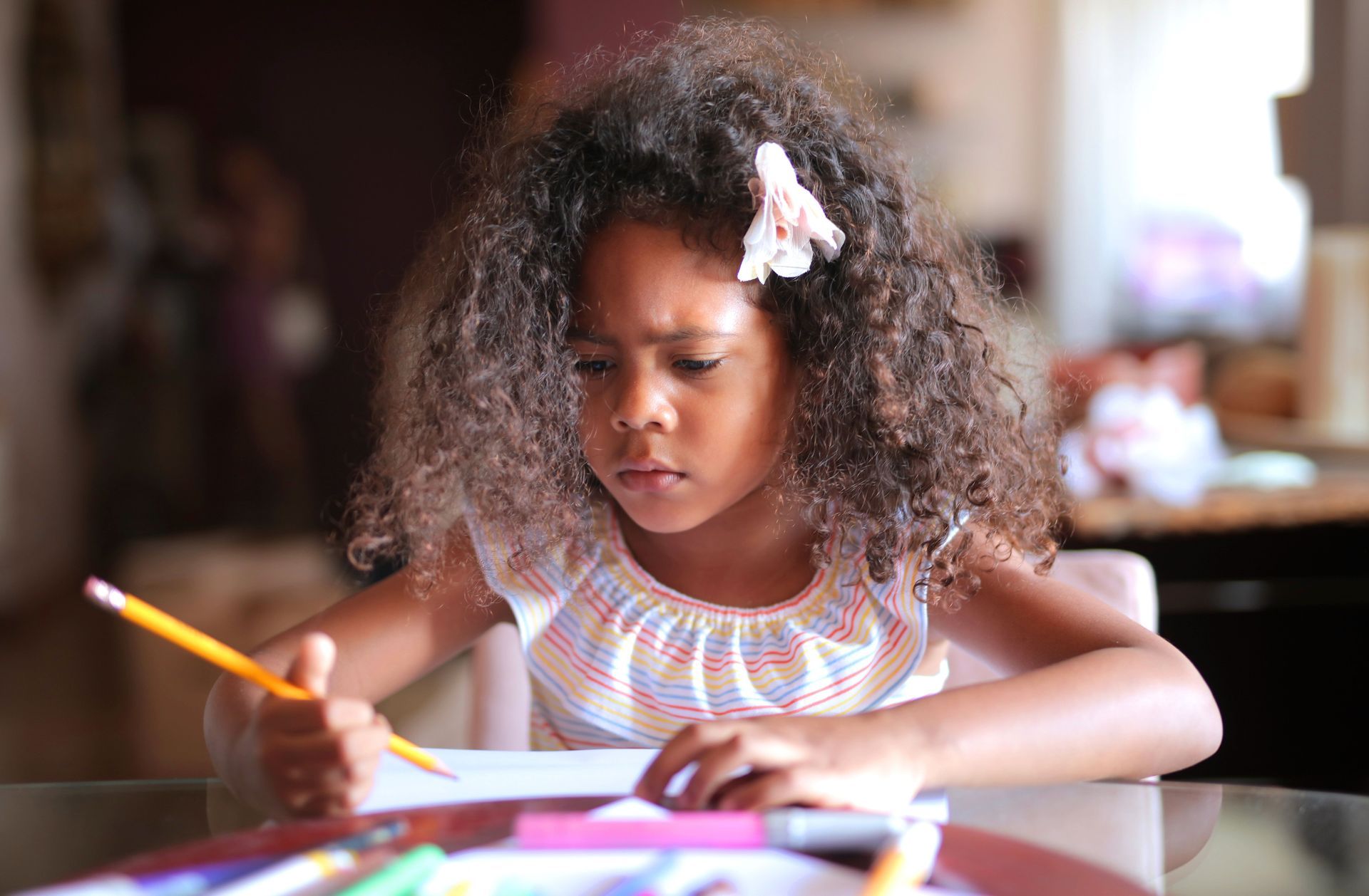 Child drawing with colored pencils at a table, concentrating on a craft project