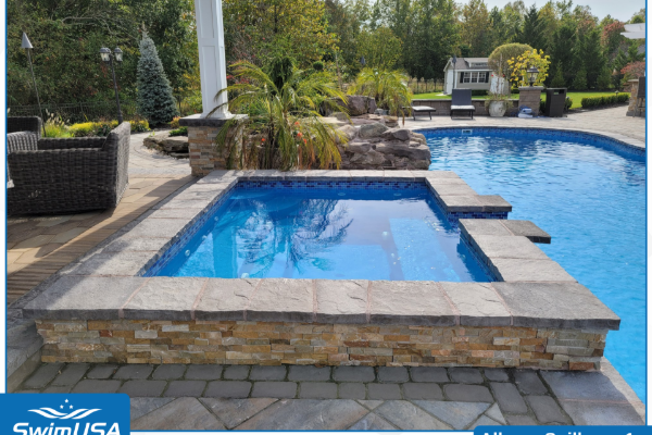 Raised spa beside a blue backyard pool with stone coping and landscaped patio