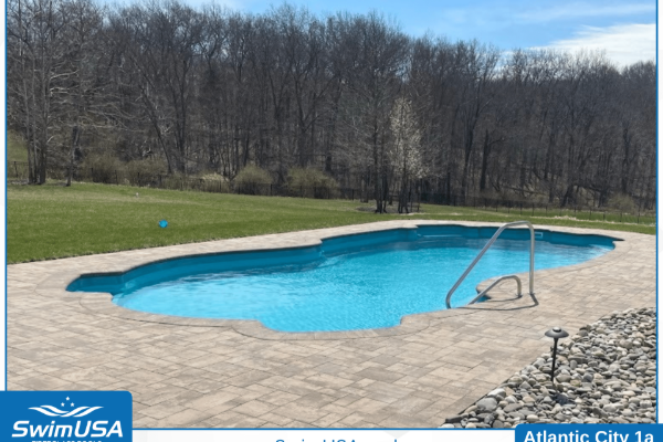 Outdoor swimming pool with blue water and a tan pool deck, set beside trees and grass