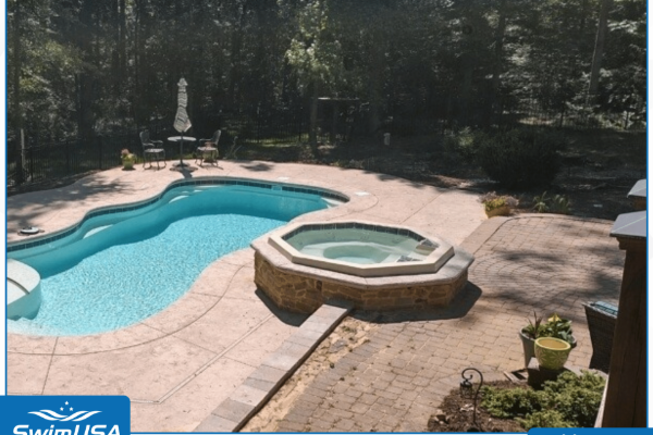 Backyard pool with attached octagonal hot tub, surrounded by stone patio and trees